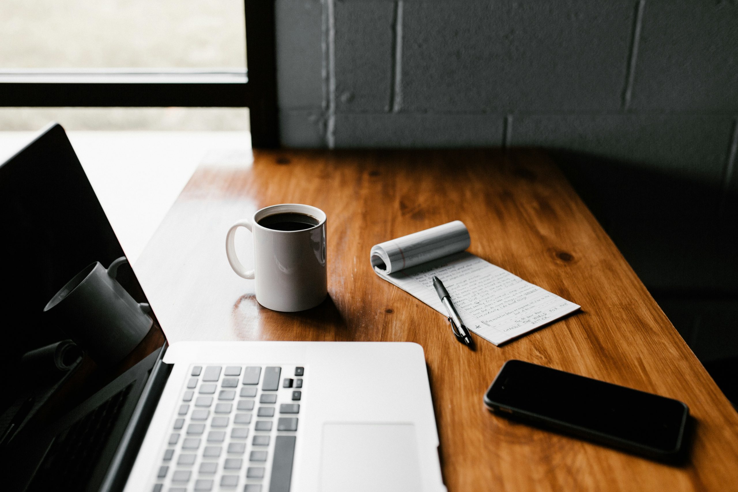 MacBook Pro, white ceramic mug,and black smartphone on tabl